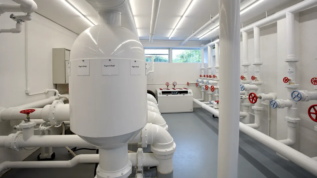 A bright, well-kept plant room: white pipework, red valve wheels, daylight from a high window.